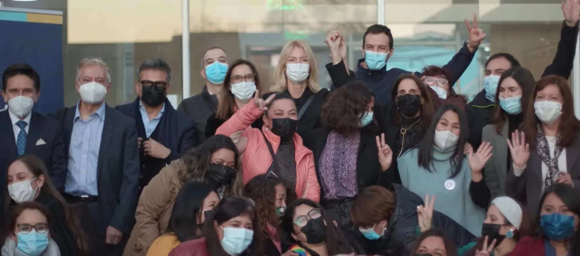 Numerosas personas con mascarillas sanitarias posan en grupo haciendo señales de victoria con las manos.