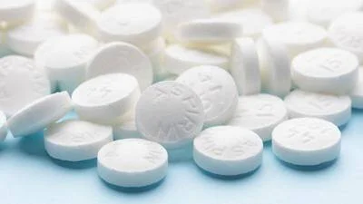 Múltiples comprimidos blancos de aspirina esparcidos sobre una superficie azul clara.