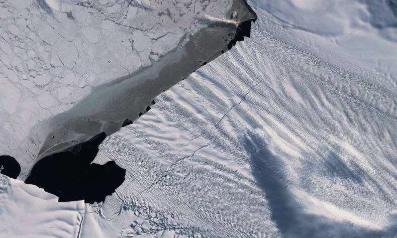 Vista aérea de una gran grieta en una plataforma de hielo polar con agua oscura expuesta entre los bloques de hielo.