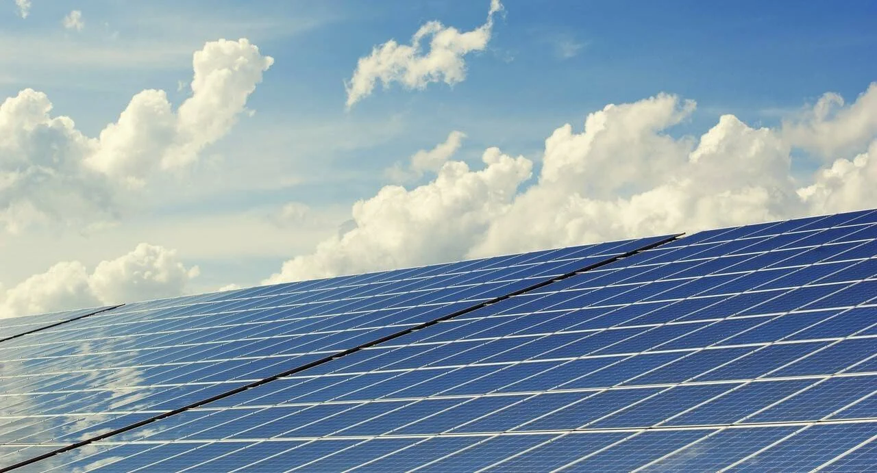 Extenso campo de paneles solares fotovoltaicos orientados hacia el cielo azul con nubes blancas.