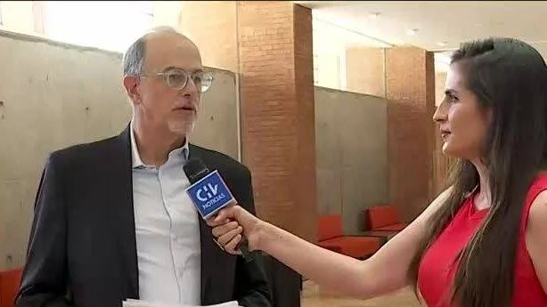Una periodista con micrófono de CIV Noticias entrevista a un hombre de traje en un interior.