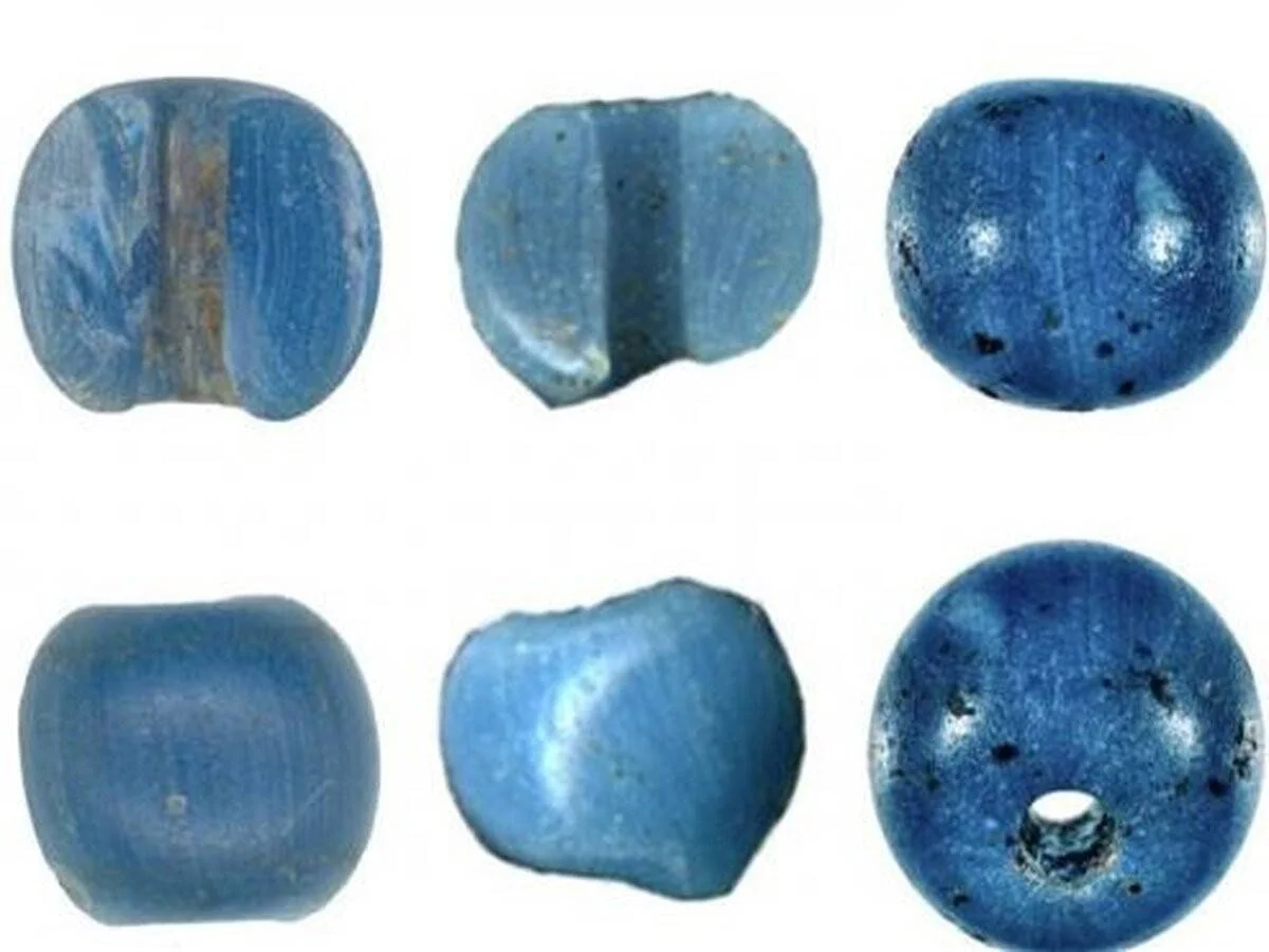Seis cuentas de vidrio azul de origen arqueológico fotografiadas desde distintos ángulos, mostrando su textura y perforaciones.