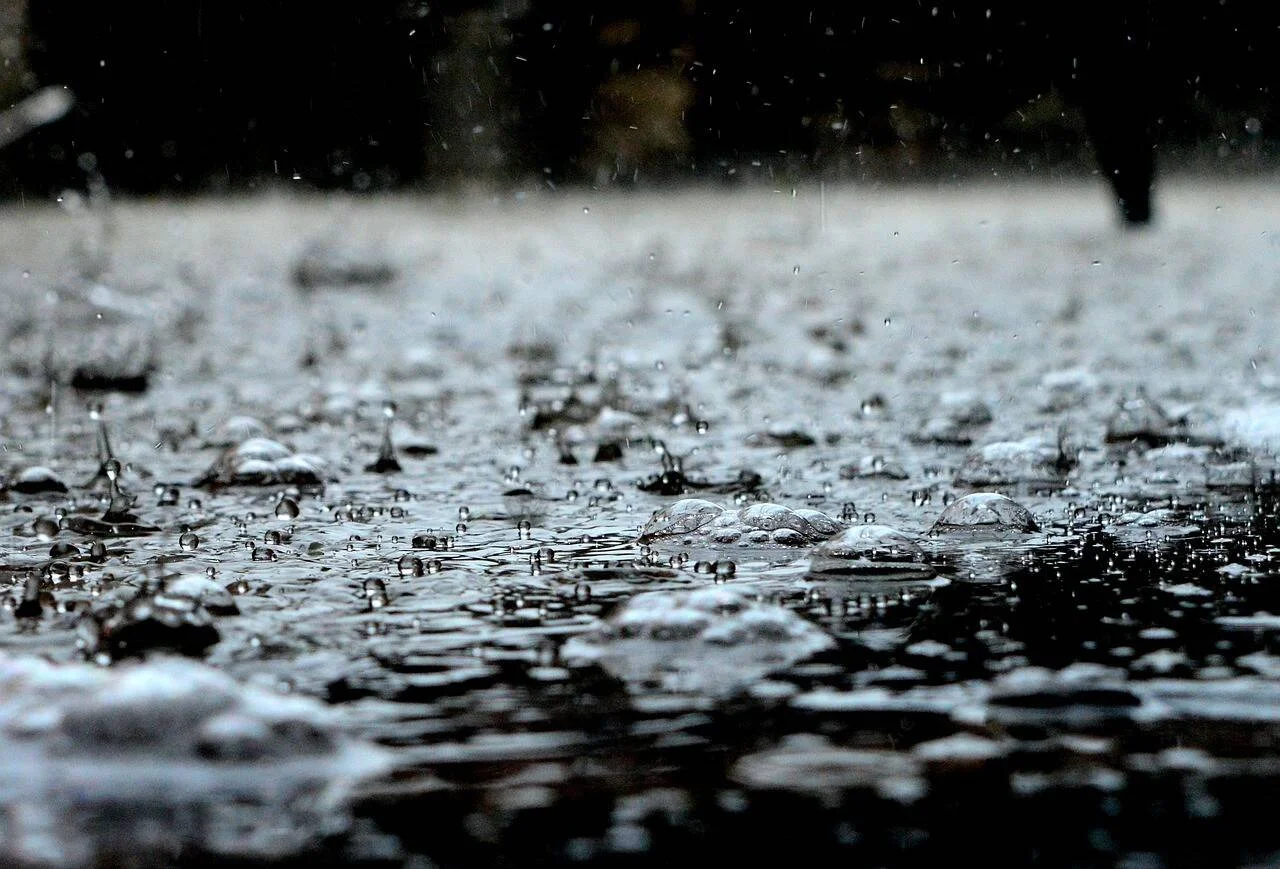 Lluvia fuerte golpeando el suelo inundado, con burbujas y salpicaduras de agua visibles a ras de suelo.