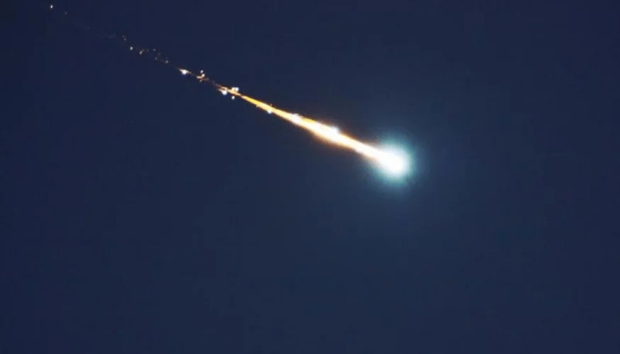 Brillante bola de fuego con estela naranja y azul atraviesa el cielo oscuro de noche.