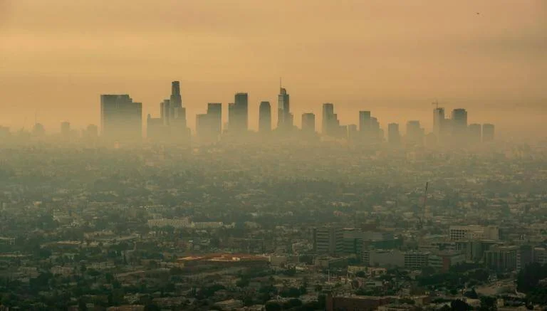 Vista aérea de una gran ciudad cubierta por una densa capa de smog naranja que difumina los rascacielos del centro.