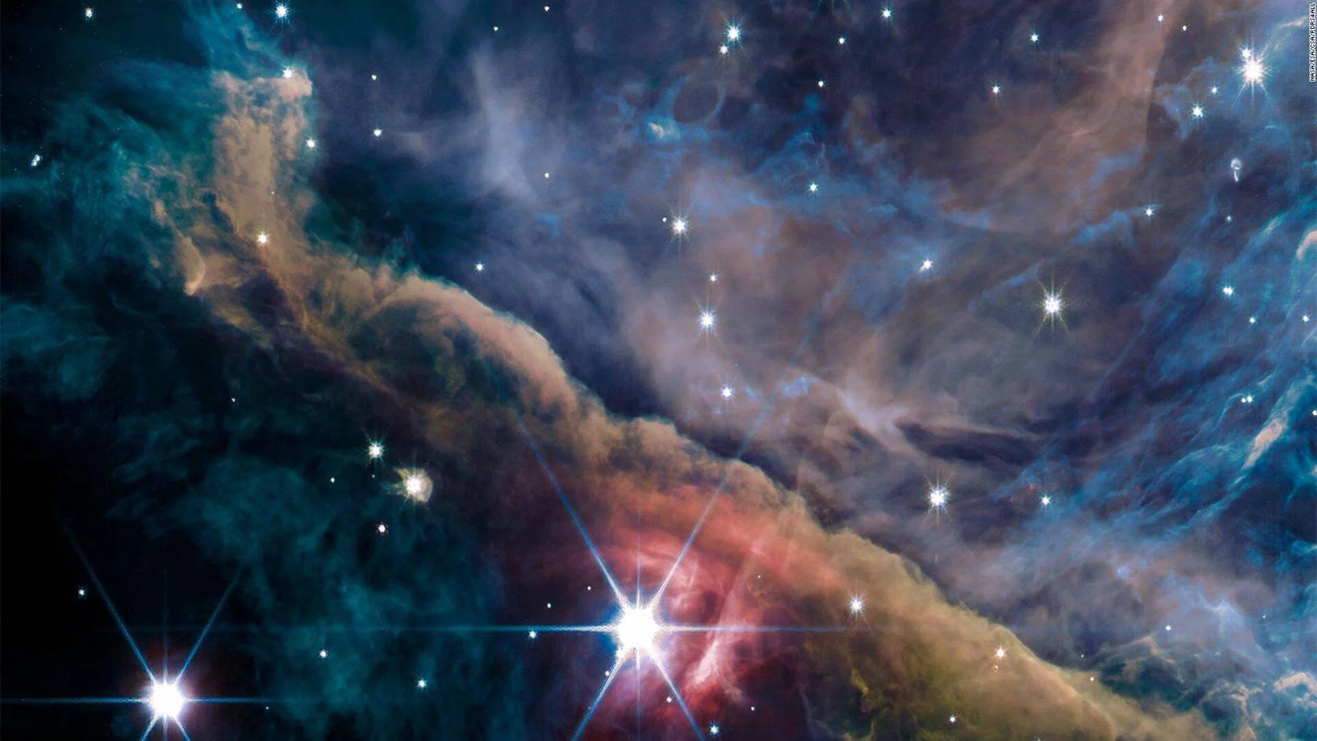 Nebulosa espacial con nubes de gas en tonos azul, rojo y dorado, salpicada de estrellas brillantes captadas por telescopio.