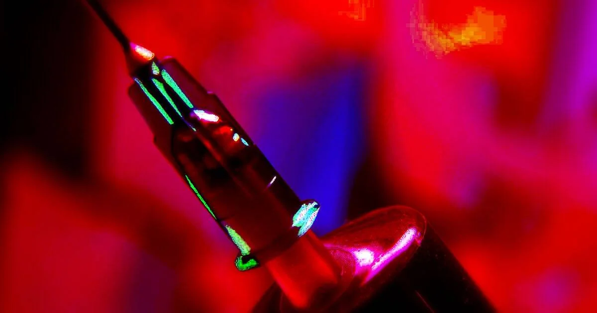 Primer plano de una jeringa médica bajo luces de colores rojo, azul y verde con efecto artístico.