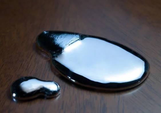 Gotas de mercurio líquido plateado y brillante derramadas sobre una superficie de madera oscura.