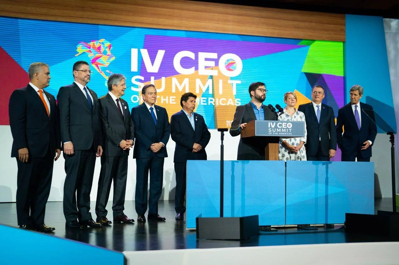 Grupo de líderes y funcionarios en el escenario del IV CEO Summit of the Americas, con un orador en el podio central.