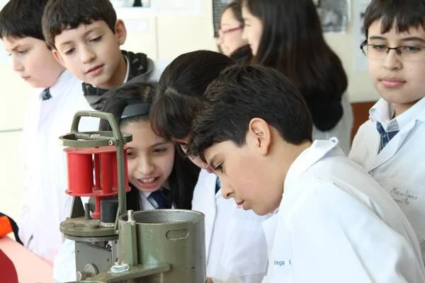 Niños con guardapolvos blancos observan con curiosidad un instrumento científico durante una clase práctica.