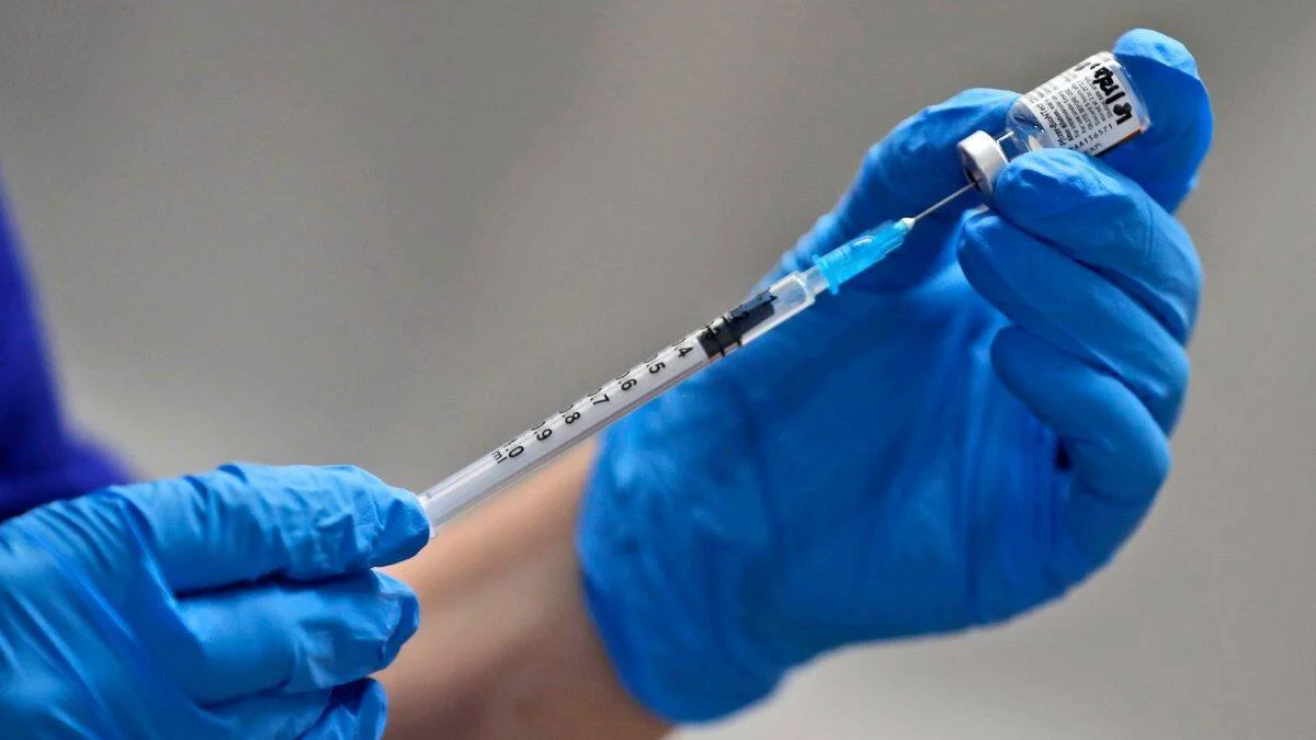 Manos con guantes azules cargan una jeringa desde un vial de vacuna.