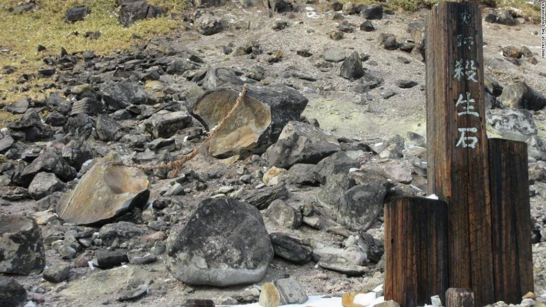 La legendaria piedra Sessho-seki aparece partida en varios fragmentos junto a un cartel de madera con caracteres japoneses en un terreno volcánico.