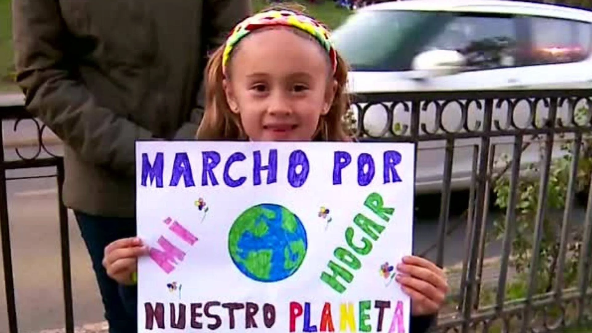 Niña sostiene un cartel hecho a mano con el mensaje 'Marcho por mi hogar, nuestro planeta' en una manifestación ambiental.