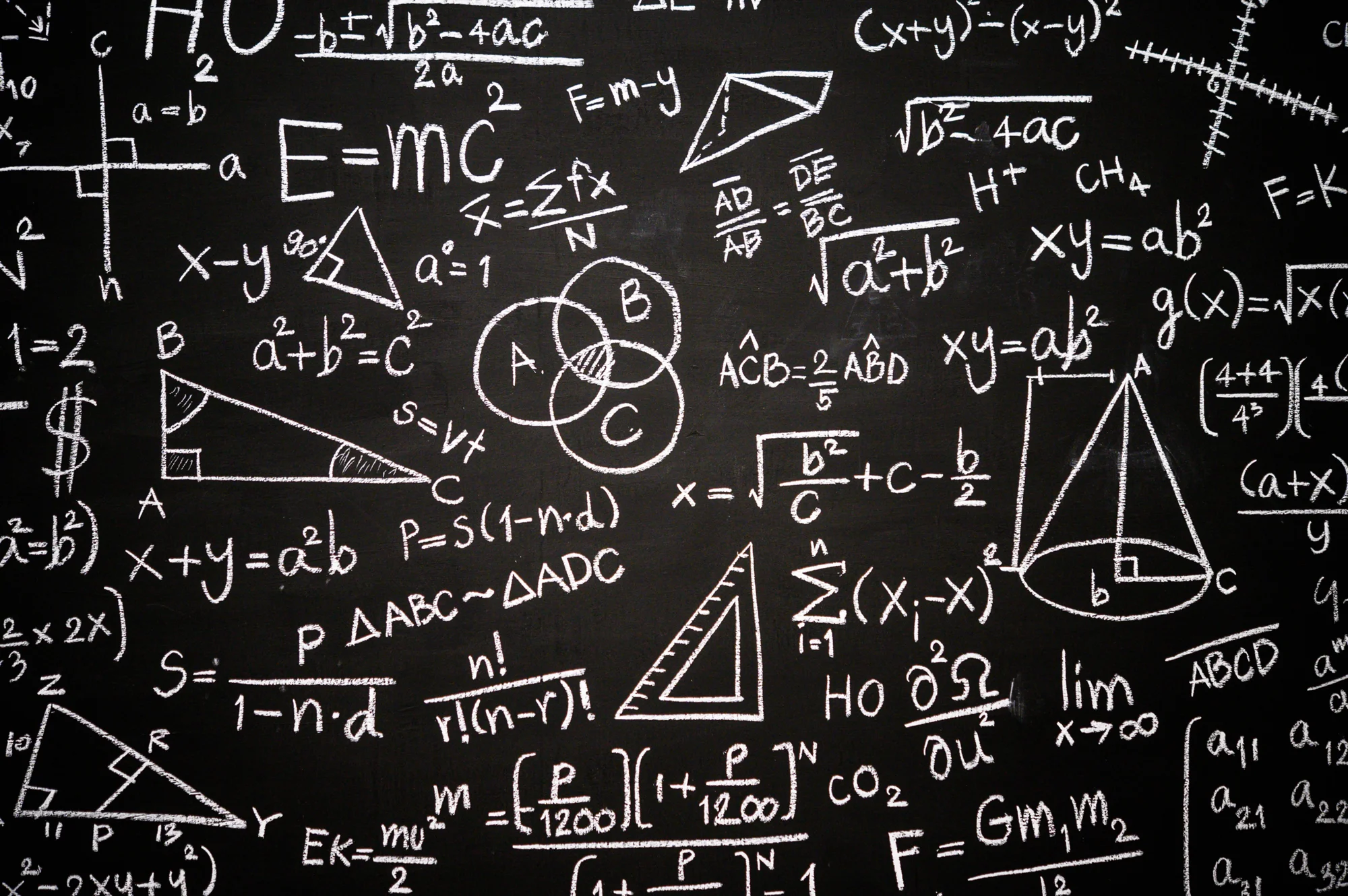 Pizarrón cubierto de fórmulas matemáticas y físicas escritas con tiza blanca, incluyendo E=mc², teorema de Pitágoras y diagramas geométricos.