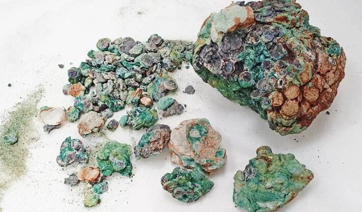 Fragmentos de roca con incrustaciones de plástico fundido de color verde y gris, conocidos como plastiglomerados, sobre fondo blanco.