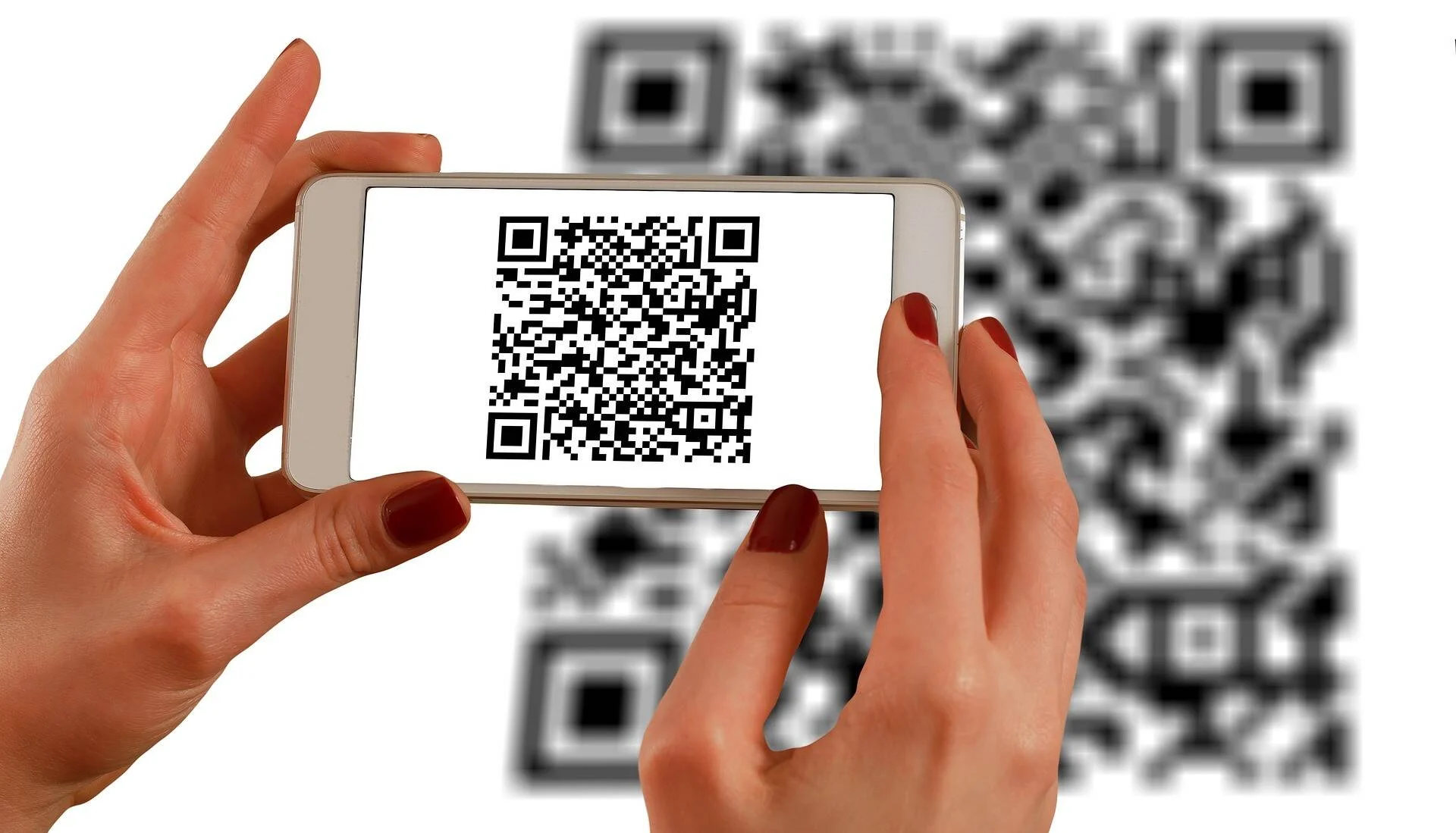 Manos sosteniendo un teléfono móvil que muestra un código QR escaneado, con otro código QR desenfocado al fondo.
