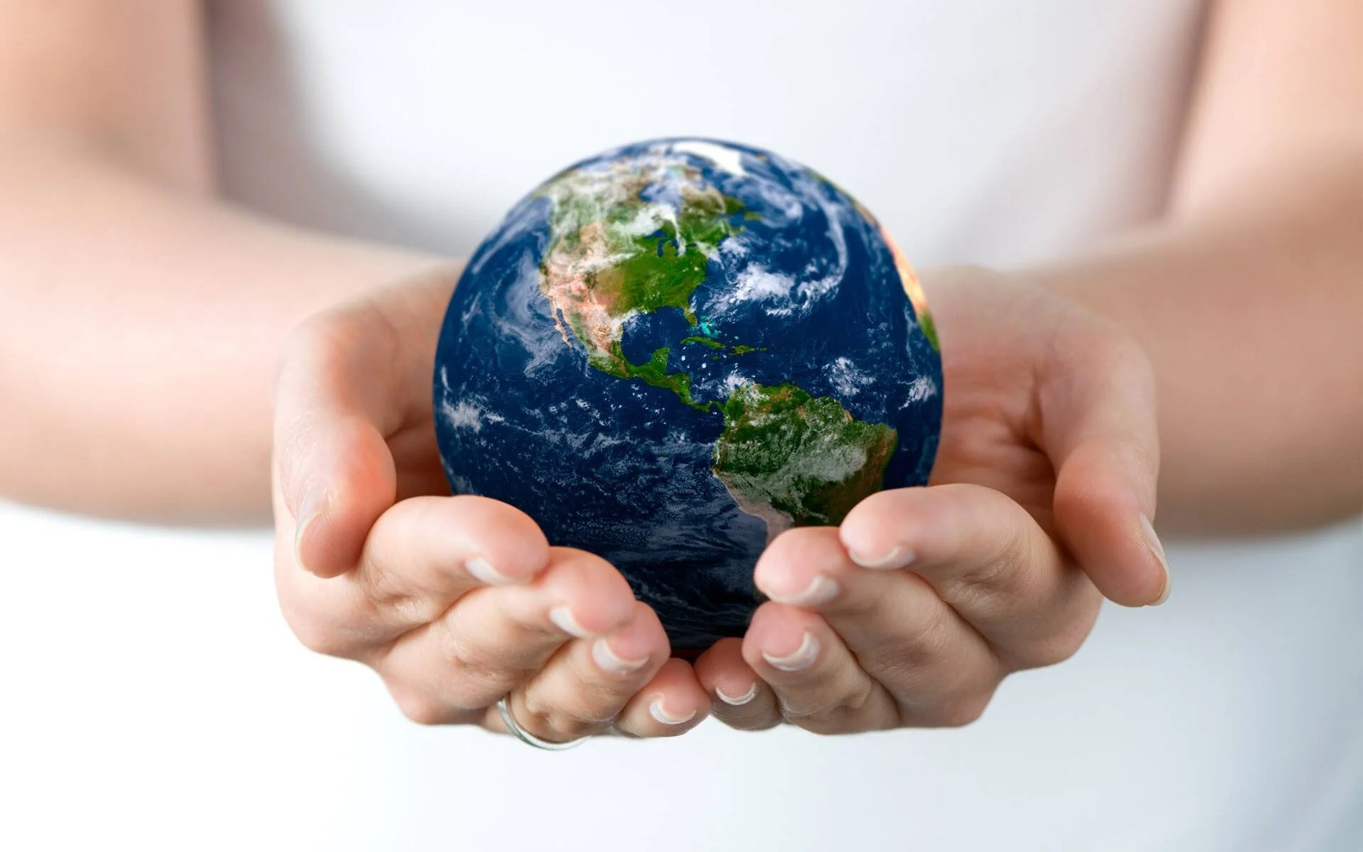 Dos manos en cuenco sostienen con cuidado una pequeña réplica del planeta Tierra, simbolizando responsabilidad ambiental.