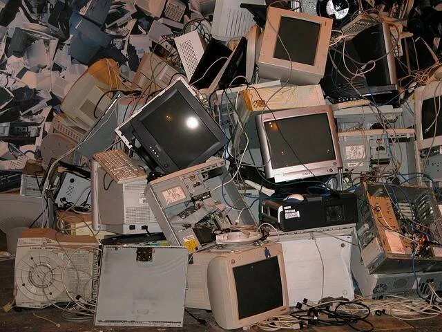 Gran pila de monitores CRT, computadoras y cables en desuso, representando basura electrónica o e-waste.