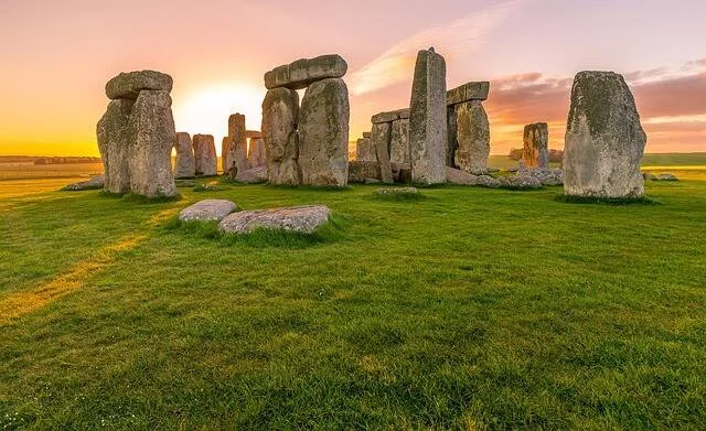 Monumento prehistórico de Stonehenge con grandes megalitos en círculo sobre pradera verde bajo un cielo al atardecer.
