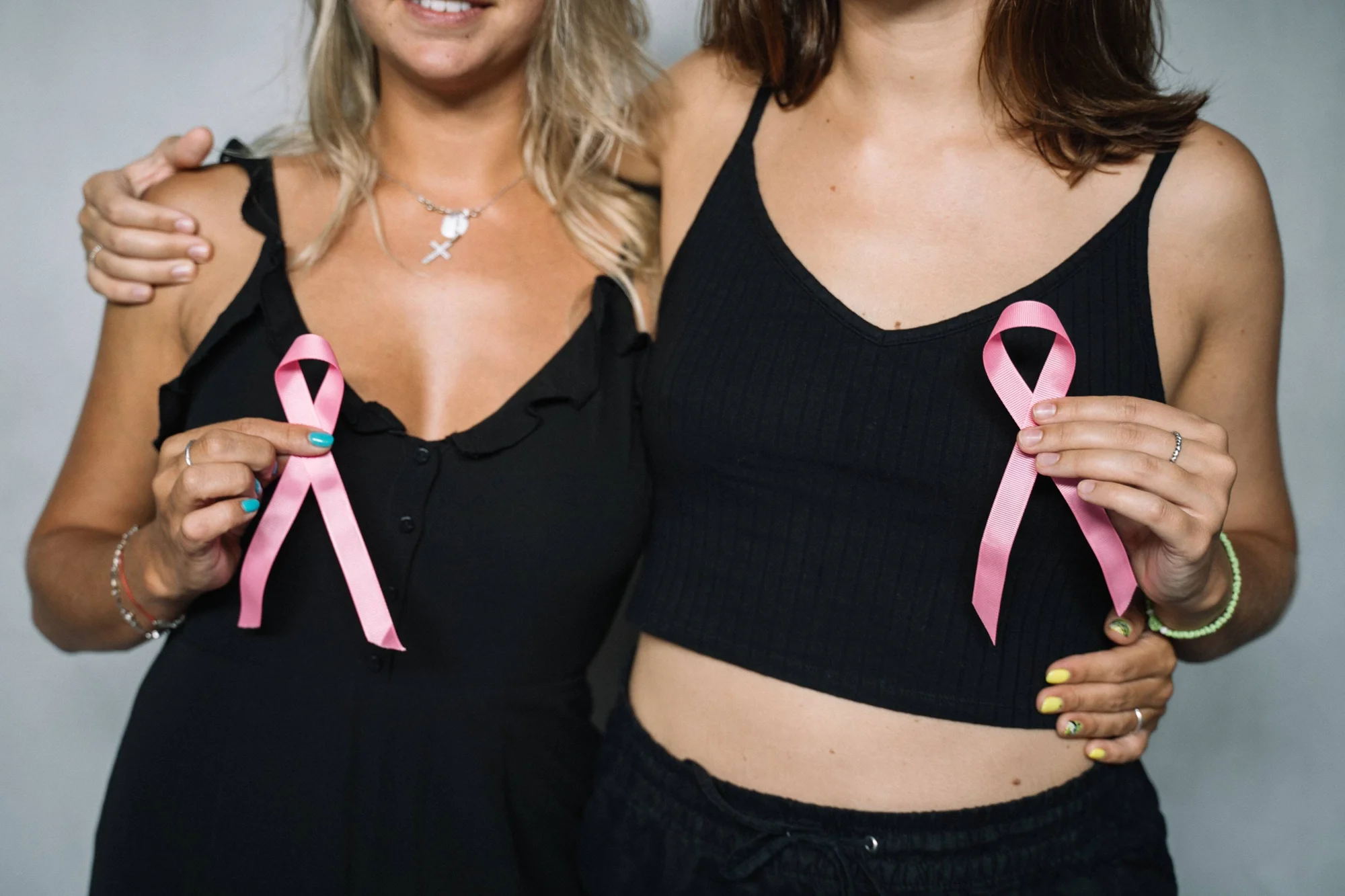 Dos mujeres vestidas de negro sostienen cada una un lazo rosa, símbolo de concientización sobre el cáncer de mama.