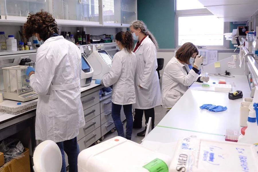 Cuatro investigadoras con batas blancas y mascarillas realizan análisis en un laboratorio equipado con instrumental científico.