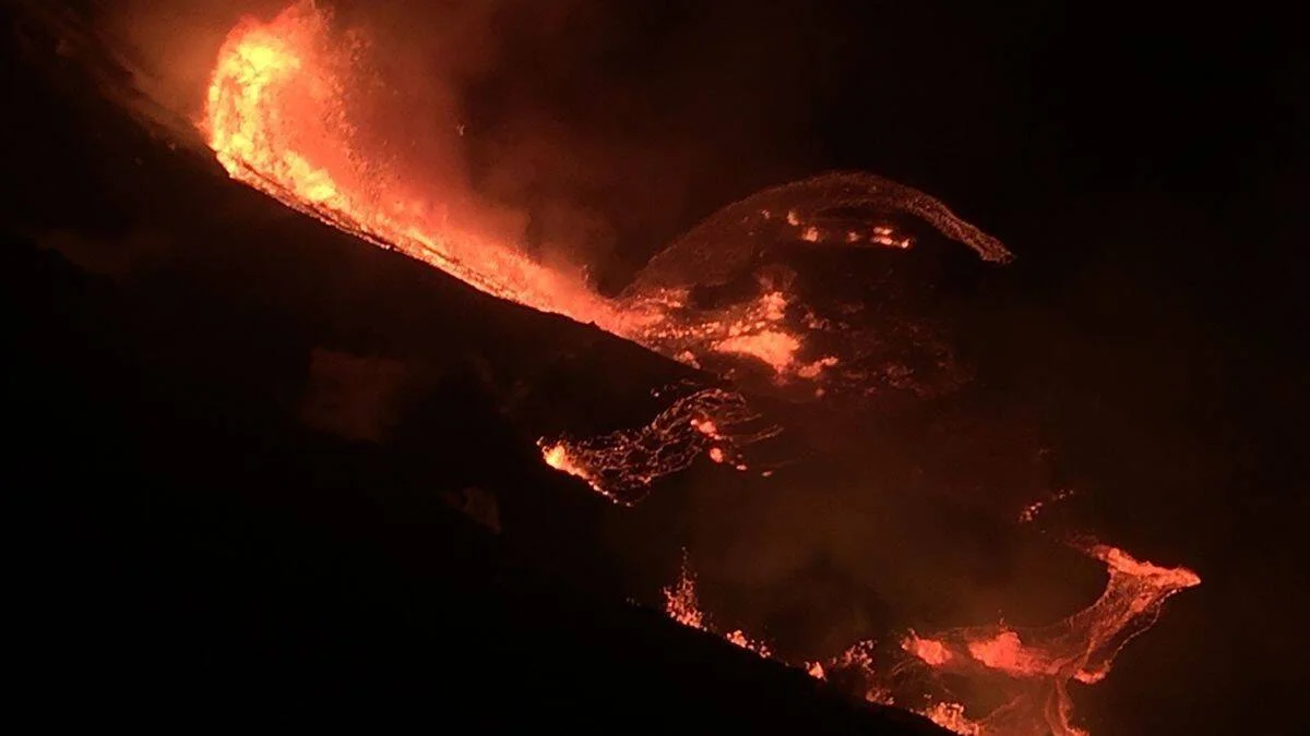 Corrientes de lava incandescente descienden por la ladera de un volcán en erupción durante la noche.