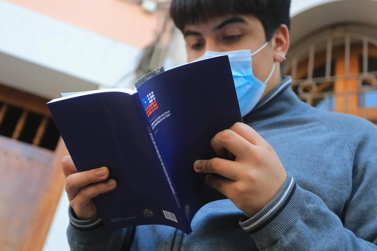 Joven con mascarilla lee el ejemplar de la Constitución Política de la República de Chile.