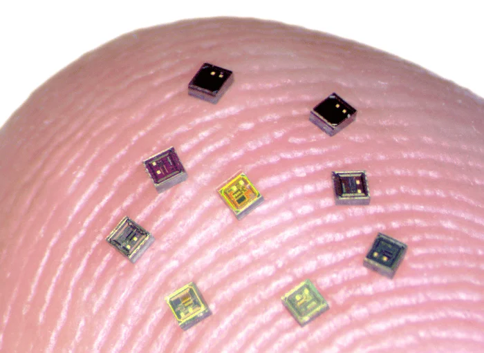 Nueve microchips de distintos colores dispersos sobre la yema de un dedo, mostrando su tamaño extremadamente reducido.