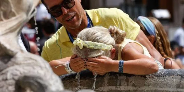 Una mujer moja su cabeza en una fuente pública mientras un hombre la asiste durante una ola de calor.
