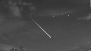 Brillante meteoro con larga estela luminosa atravesando el cielo estrellado nocturno, captado en blanco y negro.