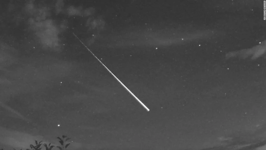 Brillante meteoro con larga estela luminosa atravesando el cielo estrellado nocturno, captado en blanco y negro.