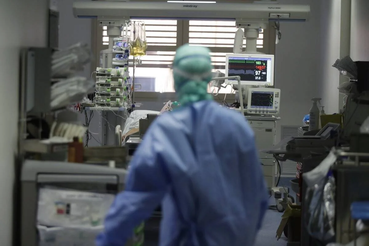 Personal médico con traje de protección atiende a un paciente en una UCI rodeada de monitores y equipos hospitalarios.