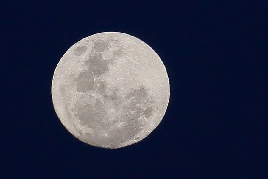 Luna llena con cráteres visibles destacándose sobre un cielo nocturno de color azul oscuro profundo.