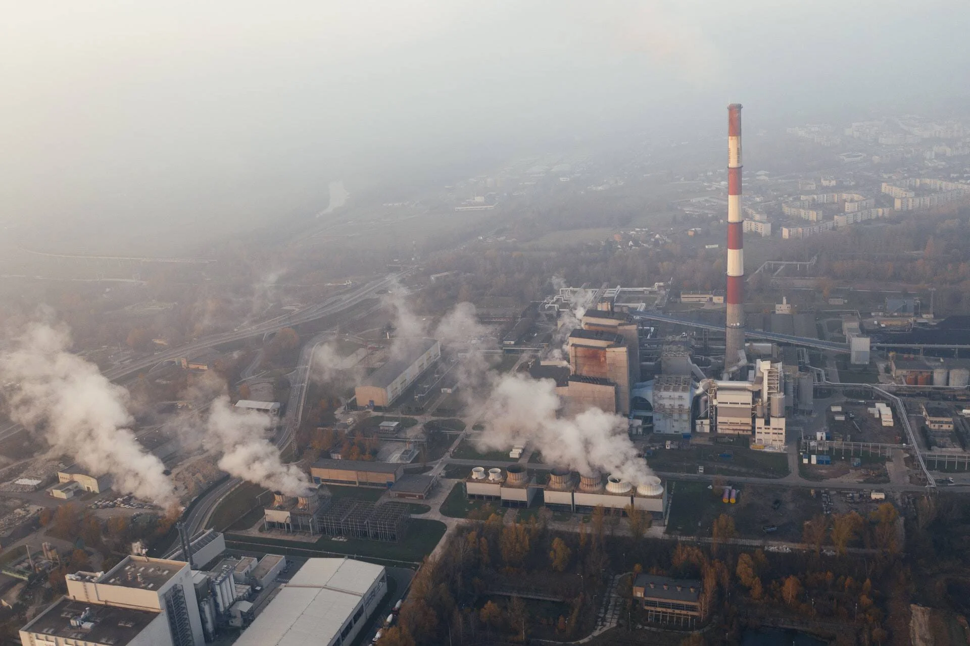 Vista aérea de una planta industrial con chimeneas emitiendo humo espeso en medio de una ciudad cubierta de smog.