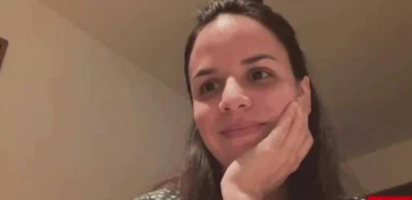 Mujer de cabello largo oscuro apoya la mejilla en su mano mientras mira hacia un lado.