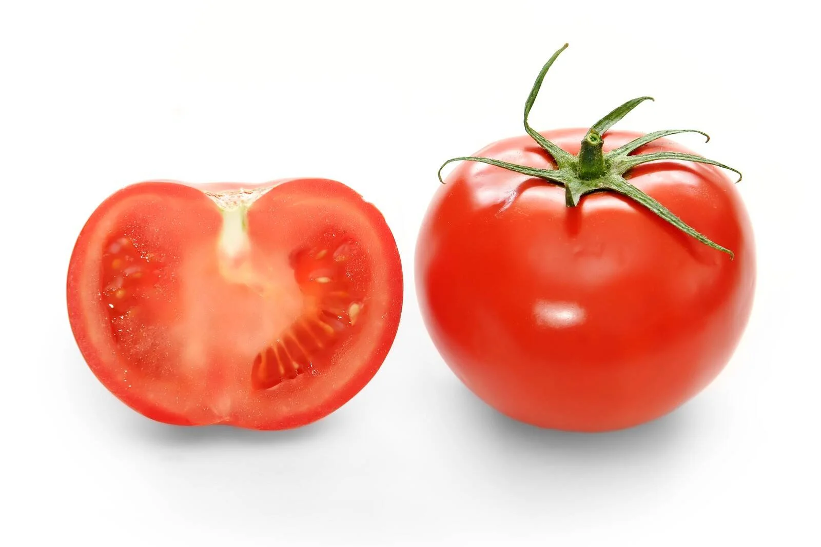 Un tomate rojo entero con tallo verde junto a una mitad que muestra su interior con semillas y pulpa.