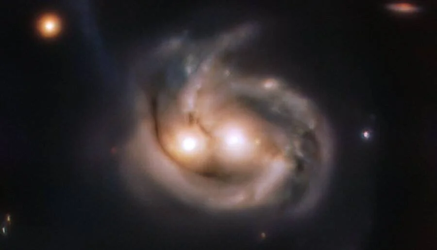 Dos galaxias en proceso de fusión captadas por telescopio, con núcleos brillantes y brazos espirales que simulan una cara sonriente.