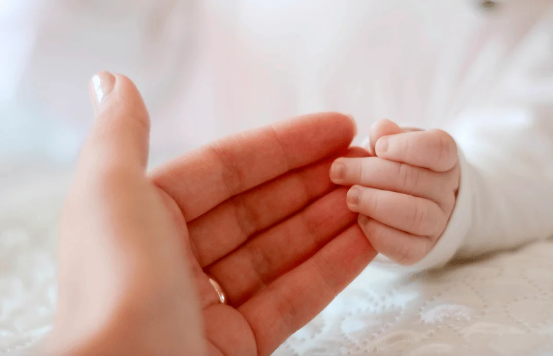 La pequeña mano de un bebé sujeta el dedo de una mano adulta, simbolizando el vínculo entre progenitor e hijo recién nacido.
