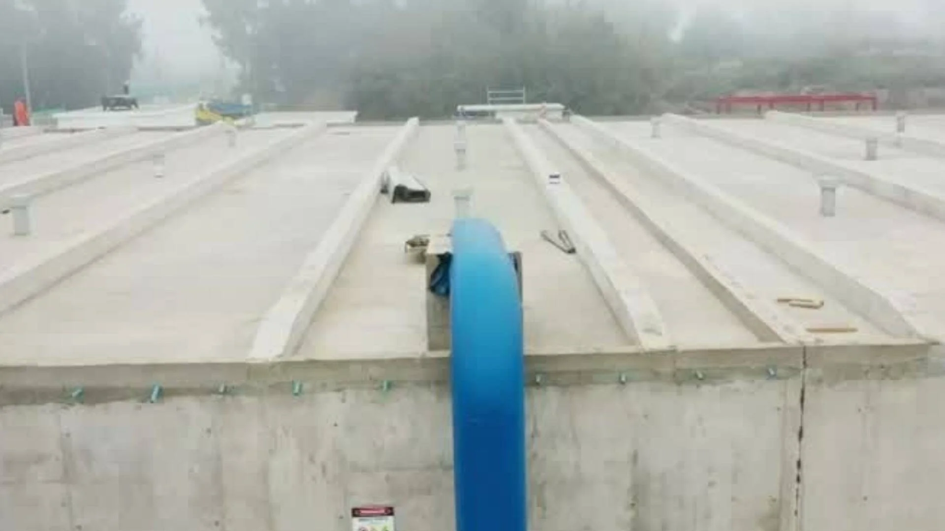 Losa de hormigón en construcción con un caño azul vertical en primer plano, rodeada de niebla.