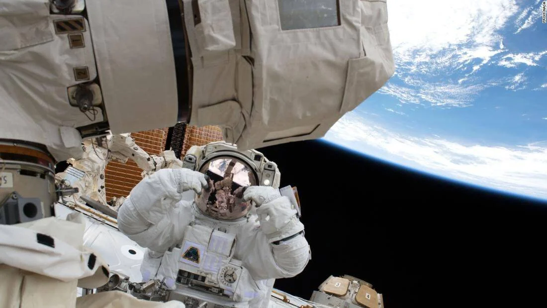 Astronauta con traje espacial realiza una caminata extravehicular junto a la Estación Espacial Internacional, con la Tierra visible al fondo.