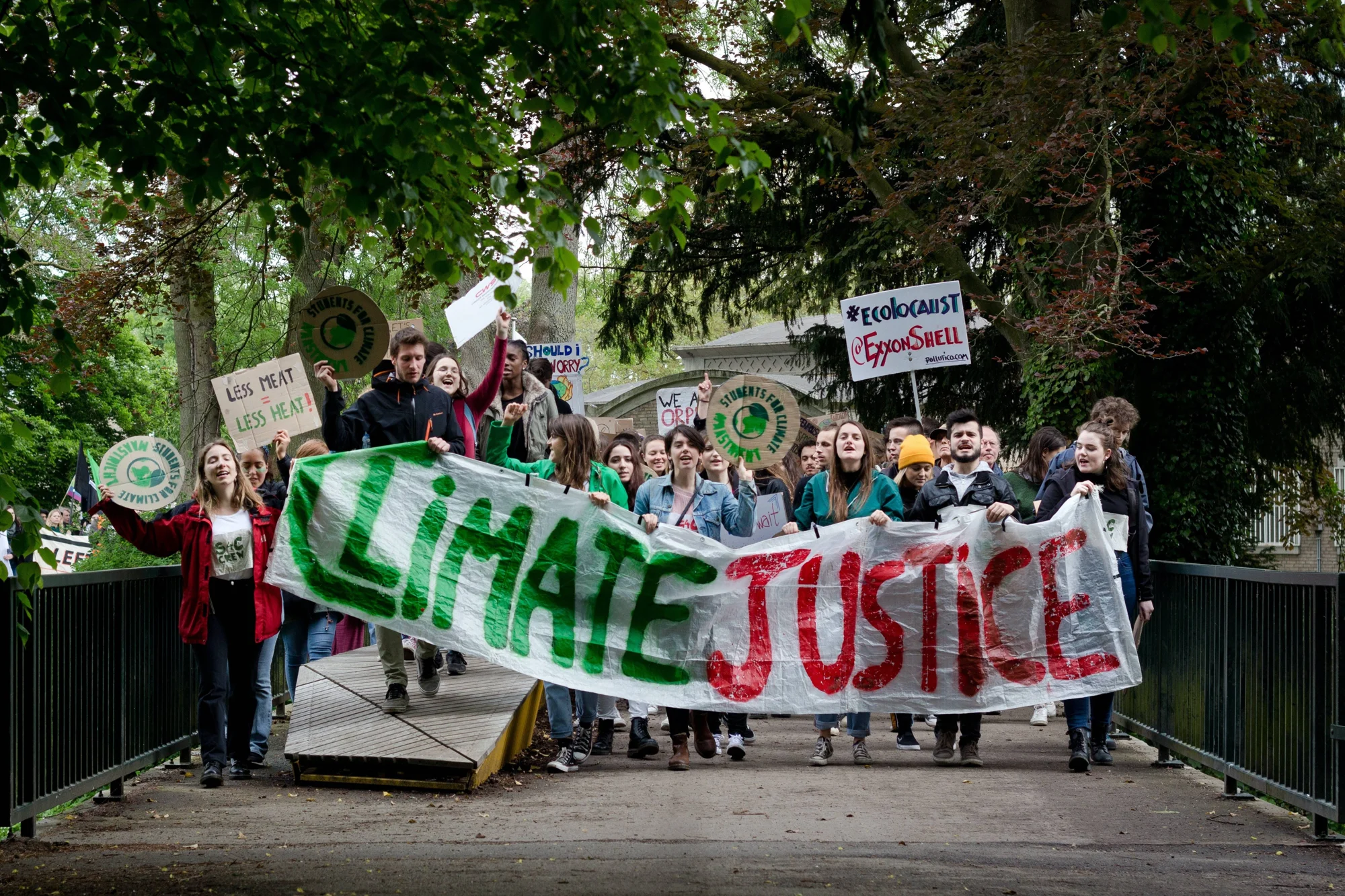 Jóvenes marchan por un puente sosteniendo una pancarta que dice 'Climate Justice' y carteles sobre el cambio climático.