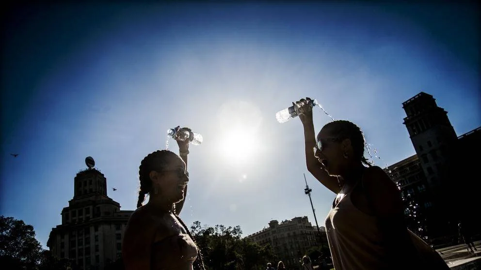 Dos mujeres se vierten agua de botellas sobre la cabeza para combatir el calor bajo un sol intenso en una ciudad.
