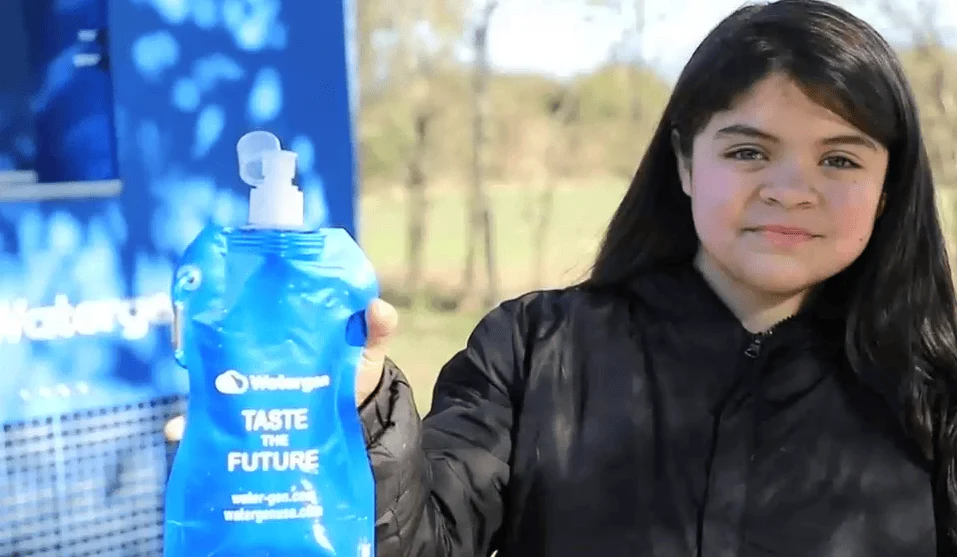 Una niña muestra una bolsa flexible azul de agua con la leyenda 'Taste the Future' de la marca Watergen.