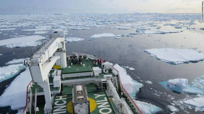 Proa de un buque científico avanzando entre fragmentos de hielo flotante en aguas polares árticas.