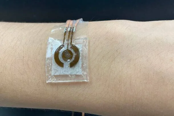 Parche sensor flexible y transparente con circuito circular adherido sobre la muñeca de una persona.