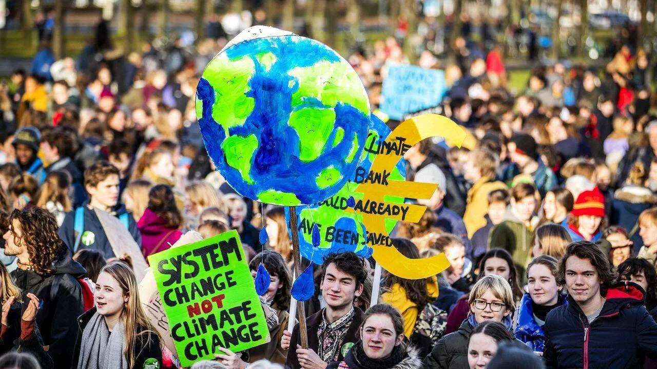 Multitud de jóvenes manifestándose por el clima con carteles que piden cambio de sistema y muestran un globo terráqueo derritiéndose.