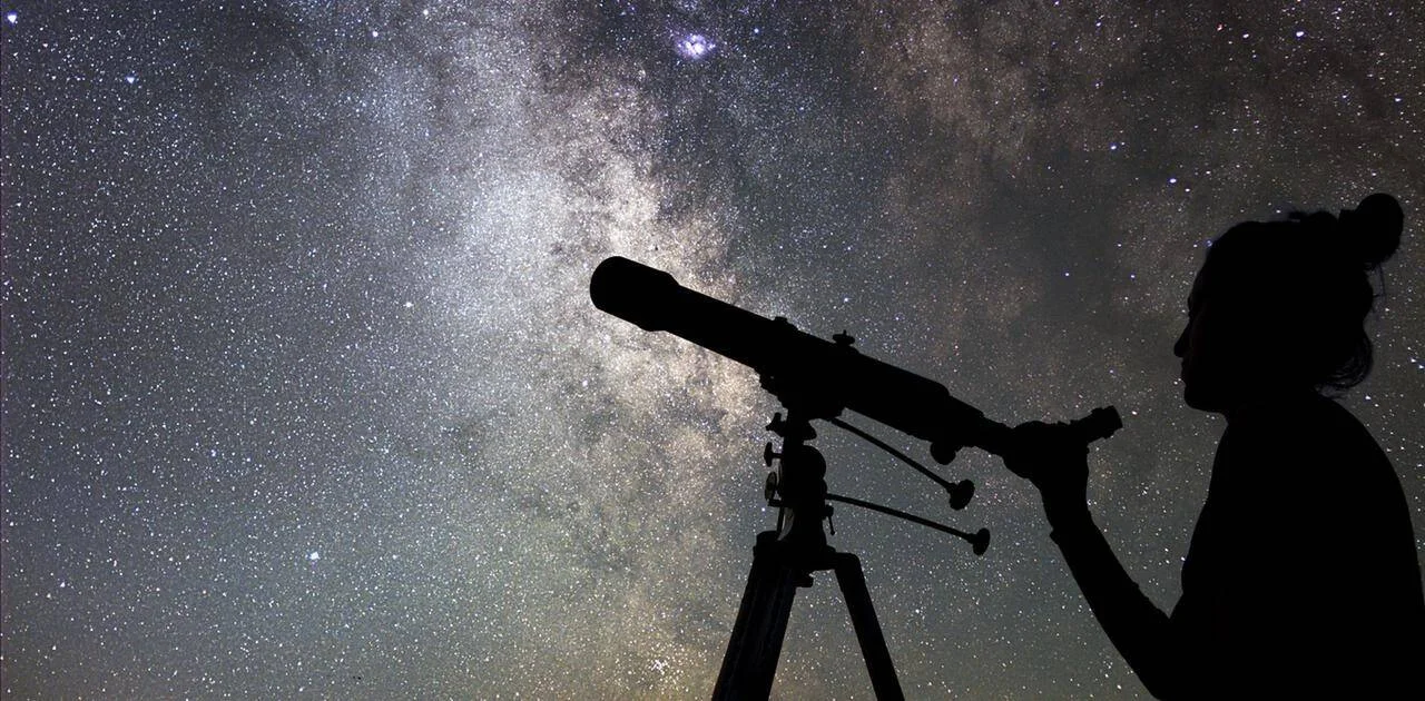 Silueta de una persona mirando por un telescopio bajo un cielo estrellado con la Vía Láctea de fondo.