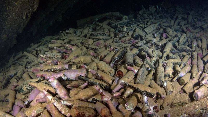 Cientos de botellas cubiertas de sedimento yacen acumuladas en el fondo del mar, posiblemente en los restos de un naufragio.