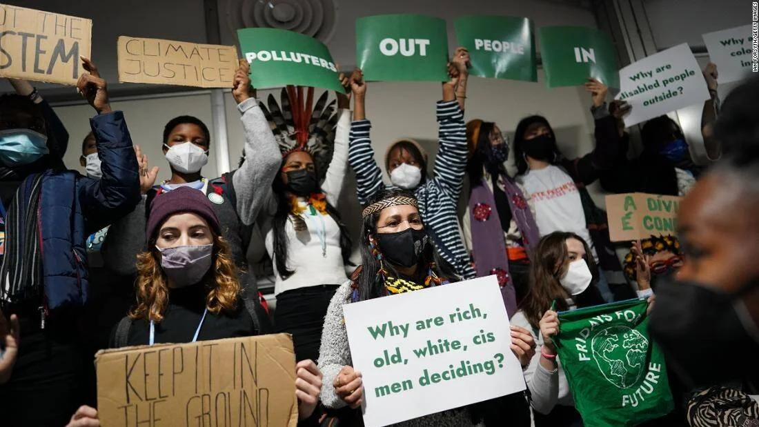 Grupo de activistas con máscaras sostiene carteles de justicia climática, incluyendo 'Polluters Out, People In' y 'Climate Justice', en una conferencia ambiental.