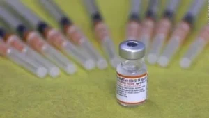 Frasco de vacuna contra el COVID-19 de Pfizer-BioNTech junto a varias jeringas cargadas sobre superficie verde.